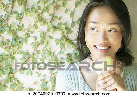 Young woman holding an apple smiling View Large Photo Image Stock Photo - Young woman holding an apple smiling. Fotosearch