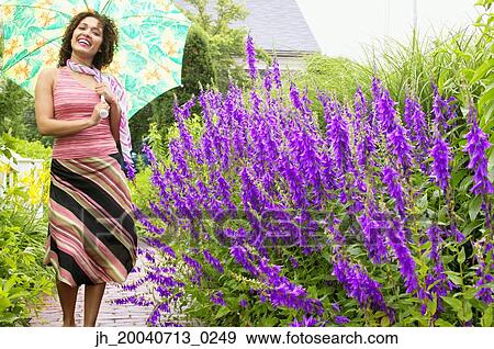 Young woman holding an umbrella standing in a garden View Large Photo Image Stock Photo - Young woman holding an umbrella standing in a garden. Fotosearch