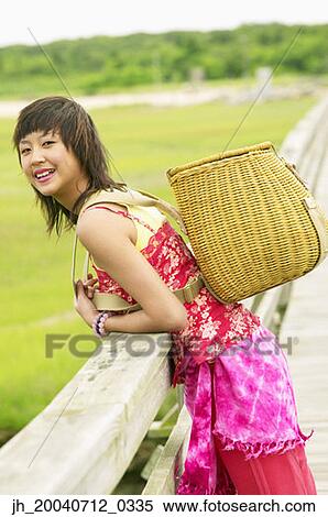 Young woman leaning over a railing on a pier holding a basket over her shoulder View Large Photo Image Stock Photography - Young woman leaning over a railing on a pier holding a basket over her shoulder. Fotosearch