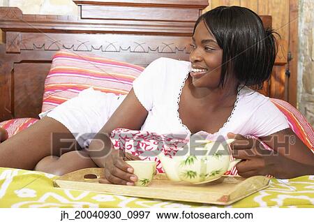 Young woman lying on a bed pouring tea from a tea pot into a cup View Large Photo Image Stock Photo - Young woman lying on a bed pouring tea from a tea pot into a cup. Fotosearch