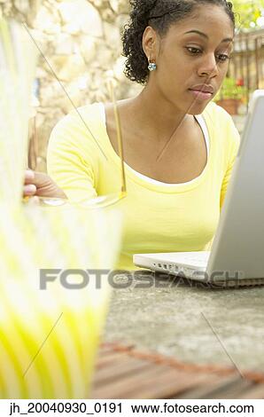 Young woman sitting at a table in front of a laptop View Large Photo Image Stock Image - Young woman sitting at a table in front of a laptop. Fotosearch
