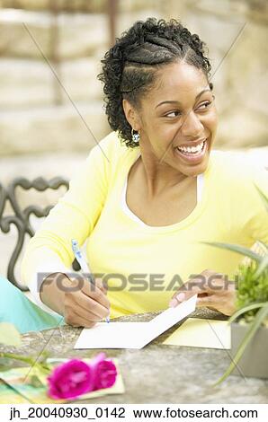 Young woman sitting at a table writing in a greeting card View Large Photo Image Stock Image - Young woman sitting at a table writing in a greeting card. Fotosearch