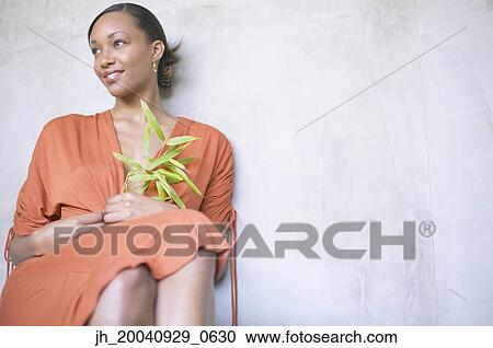 Stock Image - Young woman sitting holding a plant smiling. Fotosearch