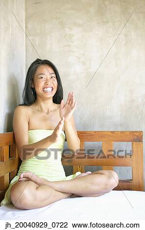 Young woman sitting on a bed clapping View Large Photo Image Stock Image - Young woman sitting on a bed clapping. Fotosearch