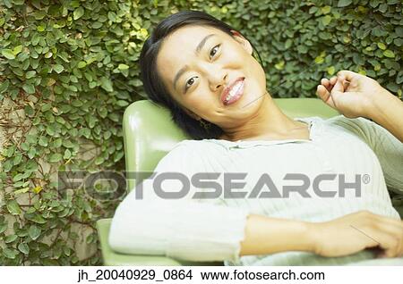 Young woman sitting on a chair outdoors smiling View Large Photo Image Picture - Young woman sitting on a chair outdoors smiling. Fotosearch