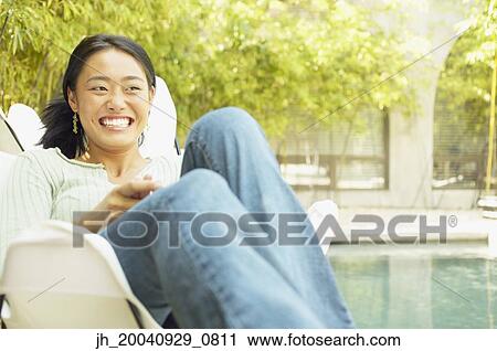 Young woman sitting on a chair outdoors smiling View Large Photo Image Stock Image - Young woman sitting on a chair outdoors smiling. Fotosearch