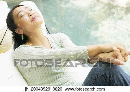 Stock Image - Young woman sitting on a chair outdoors with her eyes closed. Fotosearch