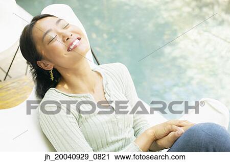 Young woman sitting on a chair outdoors smiling View Large Photo Image Stock Image - Young woman sitting on a chair outdoors smiling. Fotosearch