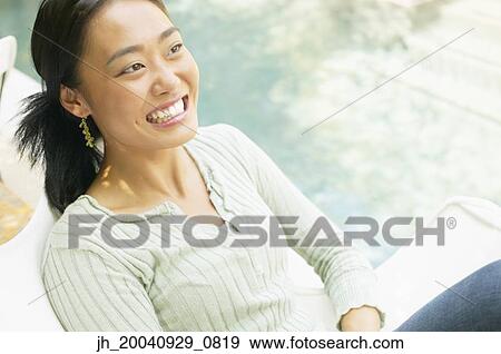 Young woman sitting on a chair outdoors smiling View Large Photo Image Stock Photo - Young woman sitting on a chair outdoors smiling. Fotosearch