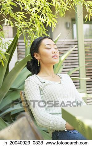 Young woman sitting on a chair outdoors with her eyes closed View Large Photo Image Stock Photo - Young woman sitting on a chair outdoors with her eyes closed. Fotosearch