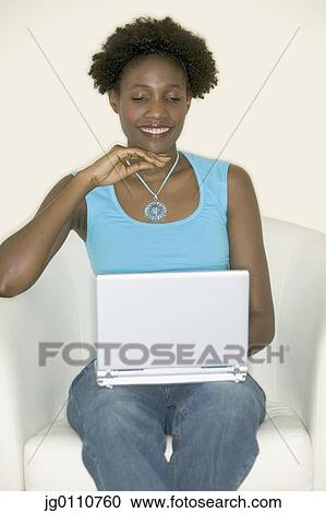 Stock Image - Young woman sitting on a couch with a laptop. Fotosearch