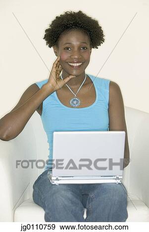 Stock Photo - Young woman sitting on a couch with a laptop. Fotosearch