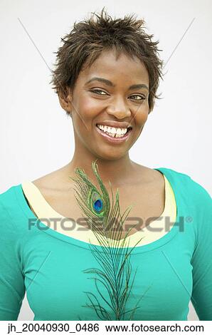 Stock Photograph - Young woman standing holding a peacock feather smiling. Fotosearch