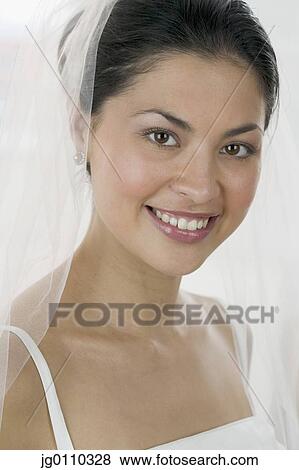Stock Photo - Young woman wearing a wedding gown looking at camera smiling. Fotosearch