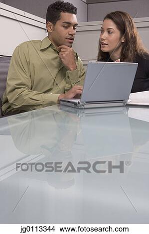 Picture - Businessman working on a laptop with a businesswoman. Fotosearch