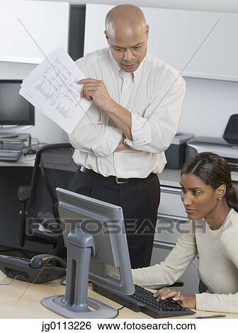 Businesswoman working on a computer a businessman standing beside her View Large Photo Image Stock Photograph - Businesswoman working on a computer a businessman standing beside her. Fotosearch