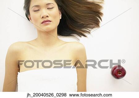 Stock Photo - High angle view of young woman lying down with her eyes closed besides an apple. Fotosearch