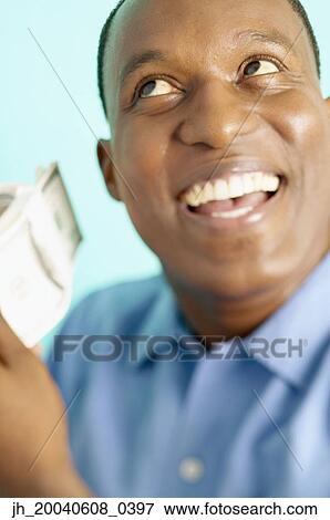 Stock Photo - Mid adult man flicking bank notes smiling. Fotosearch