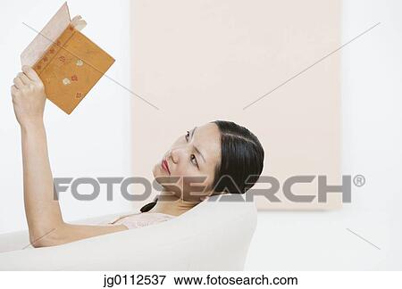 Stock Photo - Mid adult woman reading a book sitting on a couch. Fotosearch