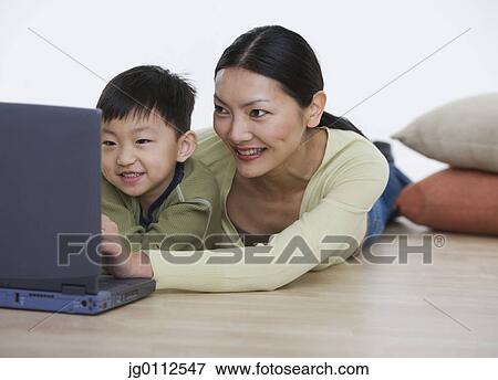 Stock Photo - Mid adult woman working on a laptop with her son. Fotosearch