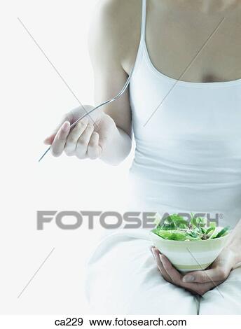 Mid section view of a young woman holding a bowl of salad and a spoon View Large Photo Image Stock Photo - Mid section view of a young woman holding a bowl of salad and a spoon. Fotosearch