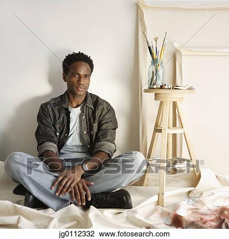 Stock Image - Portrait of a mid adult man sitting on the floor. Fotosearch