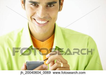 Portrait of a young man operating a hand held device View Large Photo Image Stock Photo - Portrait of a young man operating a hand held device. Fotosearch