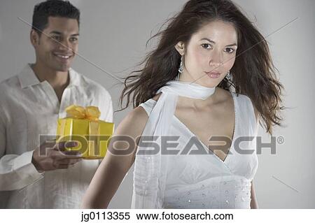 Portrait of a young man standing behind a young woman holding a gift View Large Photo Image Stock Photography - Portrait of a young man standing behind a young woman holding a gift. Fotosearch
