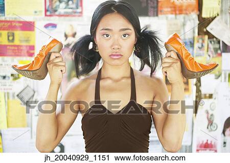 Stock Image - Portrait of a young woman holding high heel shoes. Fotosearch
