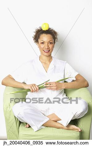 Portrait of a young woman sitting on a couch balancing an apple on her head View Large Photo Image Stock Photography - Portrait of a young woman sitting on a couch balancing an apple on her head. Fotosearch