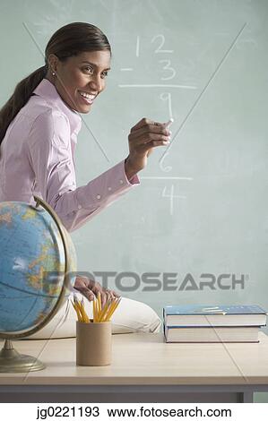 Side profile of a teacher sitting on a table in front of a blackboard View Large Photo Image Stock Image - Side profile of a teacher sitting on a table in front of a blackboard. Fotosearch