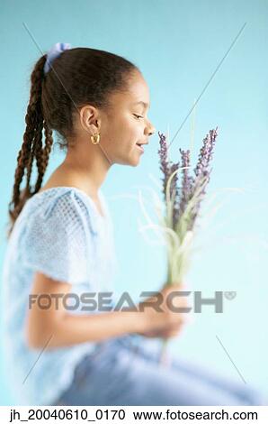 Stock Image - Side profile of a young girl smelling flowers. Fotosearch