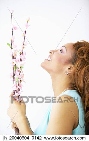 Stock Image - Side profile of a young woman holding a flower stalk. Fotosearch