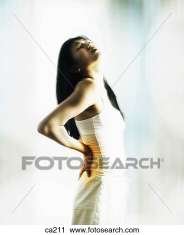Stock Image - Side profile of a young woman suffering from a backache. Fotosearch