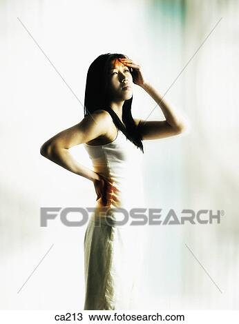 Stock Image - Side profile of a young woman suffering from a headache and a backache. Fotosearch