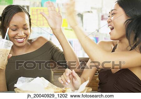 Two young woman sitting at a table eating View Large Photo Image Stock Image - Two young woman sitting at a table eating. Fotosearch