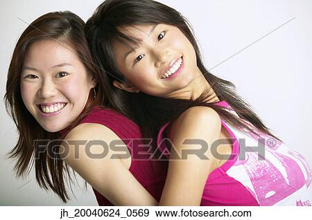 Two young women standing back to back smiling View Large Photo Image Stock Photo - Two young women standing back to back smiling. Fotosearch