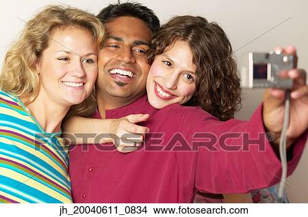 Young man and two young women taking a photograph of themselves View Large Photo Image Picture - Young man and two young women taking a photograph of themselves. Fotosearch