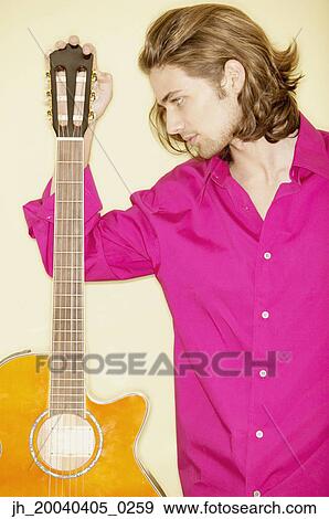 Young man holding a guitar View Large Photo Image Stock Photo - Young man holding a guitar. Fotosearch