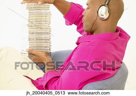 Young man sitting on a couch holding a stack of cds View Large Photo Image Stock Image - Young man sitting on a couch holding a stack of cds. Fotosearch
