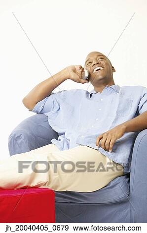Young man sitting on a couch talking on a mobile phone View Large Photo Image Stock Photo - Young man sitting on a couch talking on a mobile phone. Fotosearch