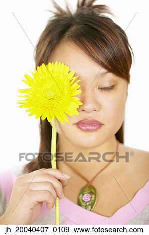 Young woman holding a flower in front of her face View Large Photo Image Stock Photo - Young woman holding a flower in front of her face. Fotosearch