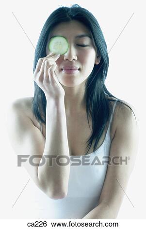 Stock Photograph - Young woman holding a slice of cucumber. Fotosearch