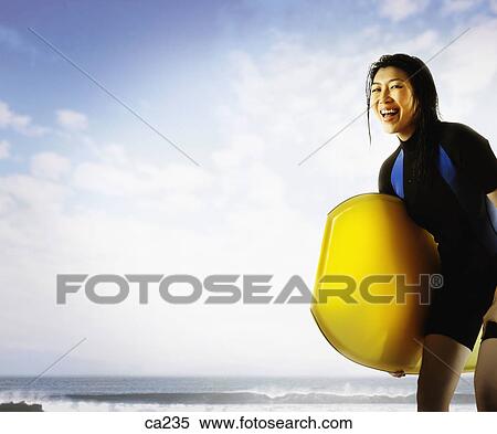 Young woman holding a surfboard on the beach View Large Photo Image Stock Photography - Young woman holding a surfboard on the beach . Fotosearch