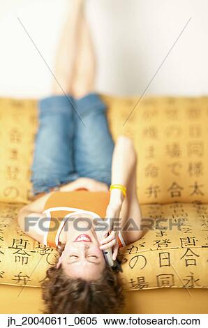 Young woman lying back on a couch talking on a mobile phone View Large Photo Image Stock Photography - Young woman lying back on a couch talking on a mobile phone. Fotosearch