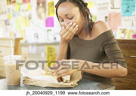 Young woman sitting at a table eating View Large Photo Image Stock Photo - Young woman sitting at a table eating. Fotosearch