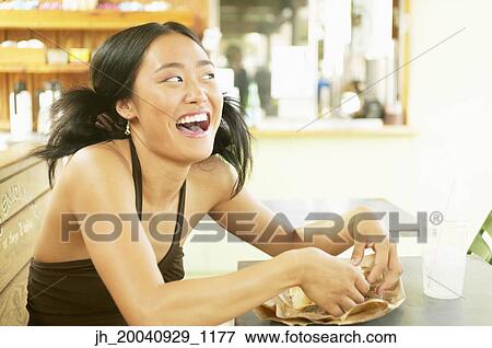 Young woman sitting at a table laughing View Large Photo Image Stock Photo - Young woman sitting at a table laughing. Fotosearch