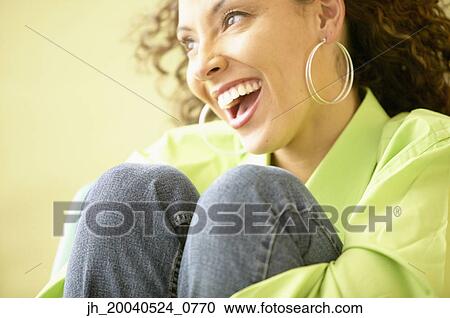 Stock Image - Young woman sitting holding her legs smiling. Fotosearch