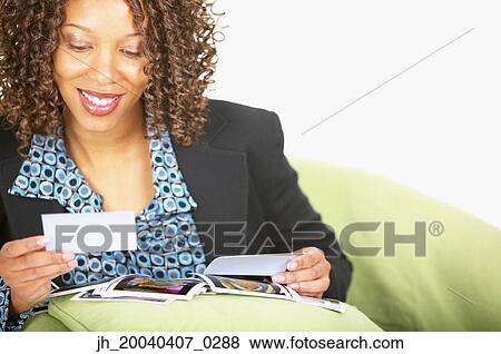 Young woman sitting on a couch at looking photographs View Large Photo Image Stock Photo - Young woman sitting on a couch at looking photographs. Fotosearch