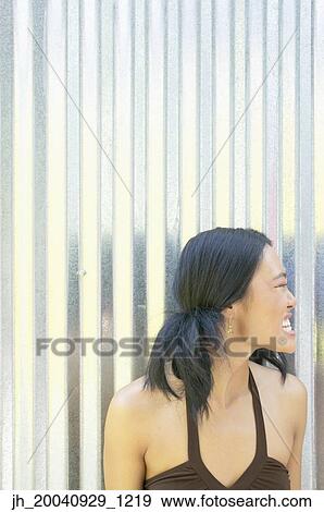 Young woman standing against a corrugated metal wall looking at the side View Large Photo Image Stock Photo - Young woman standing against a corrugated metal wall looking at the side. Fotosearch